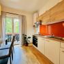Joes Cozy Aparment, © Brunner Gemütliche Küche mit Holzmöbeln, rotem Spritzschutz und Esstisch. Blick auf Balkon mit Pflanzen.