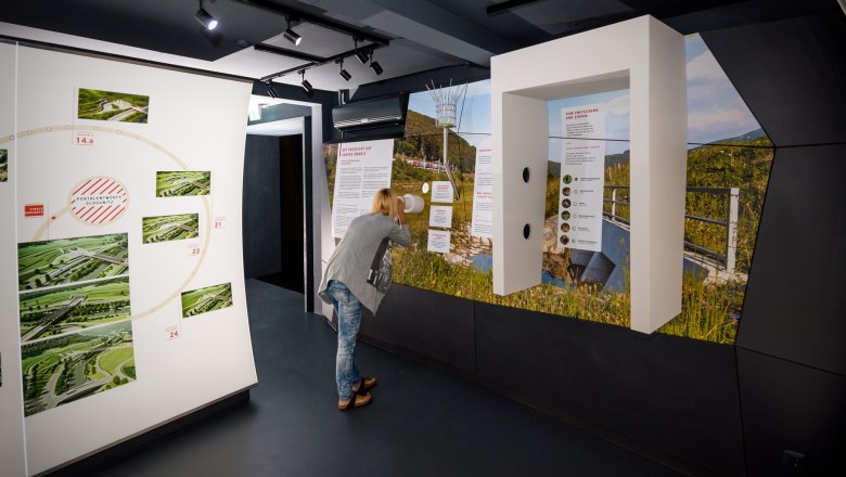 Infobox Gloggnitz, © ÖBB/grafebner Eine Person betrachtet eine Ausstellung in einem modernen Informationszentrum mit Bildern und Texten an den Wänden.