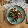 Köstlich Essen im Raxalpenhof, © Sophie Menegaldo Ein Teller mit Steak, Brokkoli, Speck und Rotkohl auf einem Tisch mit Besteck und Toast.