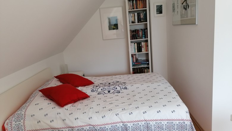 Schlafbereich im "Gartenzimmer", © Wiener Alpen Schlafzimmer mit Bett, roten Kissen und Bücherregal.