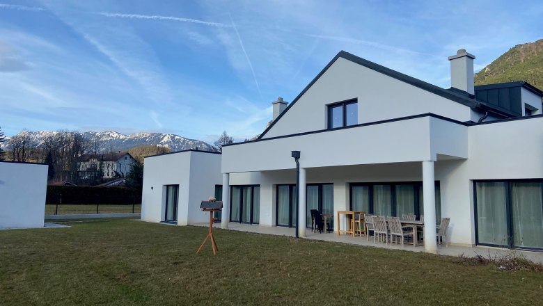 Hausansicht, © Wiener Alpen Modernes weißes Haus mit Terrasse und Garten, im Hintergrund schneebedeckte Berge.