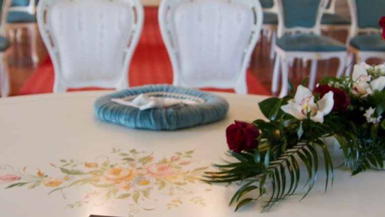 Heiraten im Schloss Gloggnitz, © Günter Brentrup Ein eleganter Raum mit weißen Stühlen und einer Trauungsmappe auf einem Tisch.