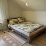 Ferienwohnungen Riedl, © Familie Riedl Ein gemütliches Schlafzimmer mit einem Doppelbett, gemusterten Bettbezügen, einem kleinen Nachttisch und einem Fenster mit Vorhängen.