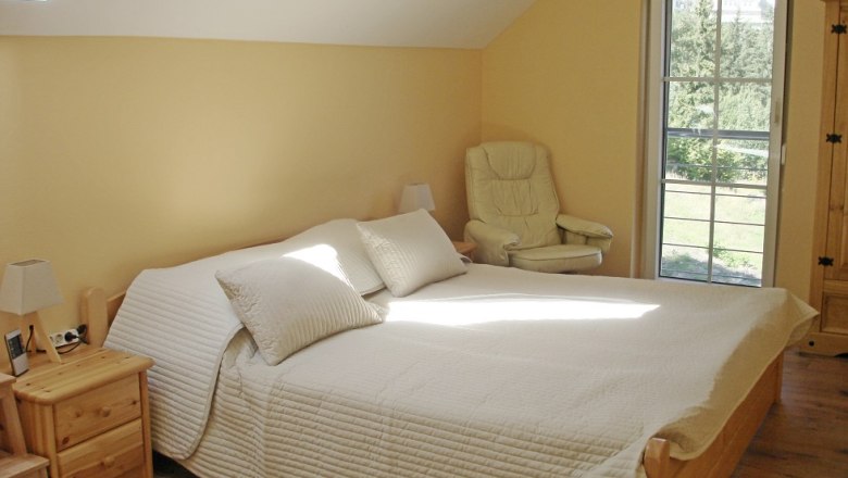 Ferienwohnung Schlafzimmer, © Vadim Drozdov Helles Schlafzimmer mit Doppelbett, Sessel und Fenster mit Blick ins Grüne.