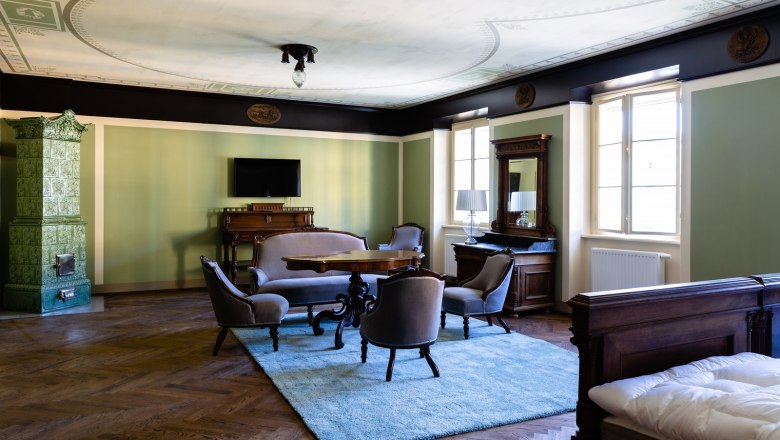 Zimmer, © Thalhof, Katrin Nusterer Elegantes Zimmer mit antiken Möbeln, grünem Kachelofen und Teppich.