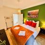 Joes Coxy Apartment, © Brunner Gemütliches Schlafzimmer mit grün gestrichener Wand, Doppelbett mit roten Kissen, Nachttischen und Lampe.