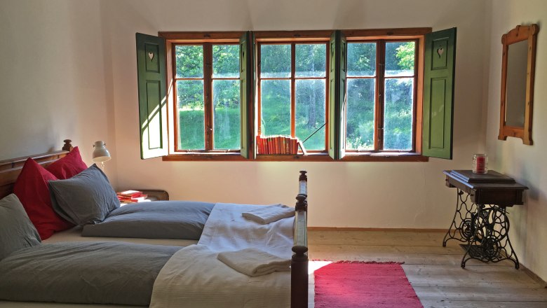 Doppelzimmer, © Riegelhof Gemütliches Doppelzimmer mit Holzboden, Bett, Fenster mit grünen Fensterläden und einem roten Teppich.