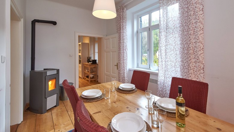 Top 1 - Esszimmer, © VP FeWo OG Esszimmer mit Holztisch, roten Stühlen, gedecktem Tisch und Kaminofen.