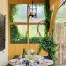 Top 1 - Terrasse, © VP FeWo OG Ein gedeckter Tisch auf einer Terrasse mit Weinflasche, Geschirr und Kerzen, umgeben von Efeu und Holzwänden.