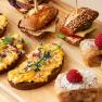 Feine Kaffeepausen bei einem Seminar, © Sporthoel Semmering Verschiedene Snacks auf einem Holzbrett, darunter belegte Brote, Sandwiches und Gebäck mit Himbeeren.