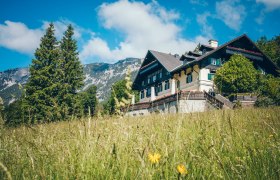 Knappenhof, © Knappenhof - Christian Husar Ein traditionelles Gebäude namens Knappenhof in einer grünen Wiese vor einer Bergkulisse.