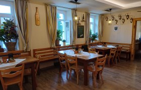 Dorfstub'n Wartmannstetten, © Wiener Alpen Innenansicht eines gemütlichen Gastraums mit Holztischen und Stühlen, dekoriert mit Pflanzen und Hirschgeweihen an der Wand.