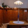 Orlet an der Rax, © Sofia Orlet Rustikaler Raum mit Holzwänden, Tisch und Bank. Vase mit blauen Blumen auf Tischdecke. Lampe mit Blumenmuster an der Decke.