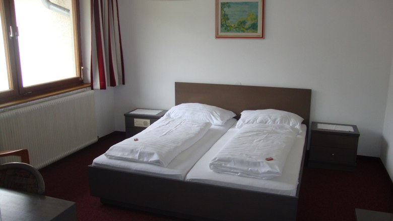 Die gemütlichen Zimmer im Gasthof-Pension Seelhofer, © Gasthof-Pension Seelhofer Ein einfach eingerichtetes Hotelzimmer mit Doppelbett, Nachttischen und einem Fenster mit Vorhängen.