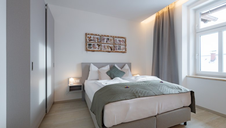 Apartment 3, © Atelier Fürtner-Ton Modernes Schlafzimmer mit Doppelbett, grauen Vorhängen und Wanddekoration.