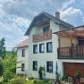 Ferienwohnungen Riedl, © Wiener Alpen Ein zweistöckiges Haus mit Balkon und Terrasse, umgeben von Garten und Bäumen, unter einem bewölkten Himmel.