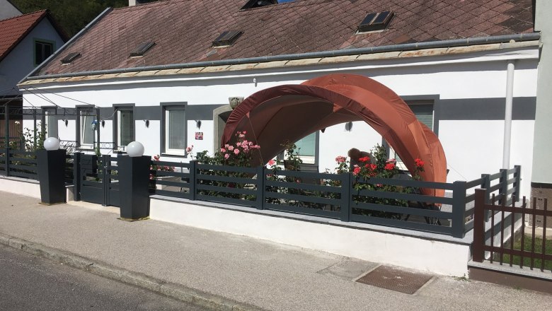 Hausansicht Rosengarten, © Familie Mitra Ein weißes Haus mit einem kleinen Garten und einem orangefarbenen Pavillon vor der Tür.