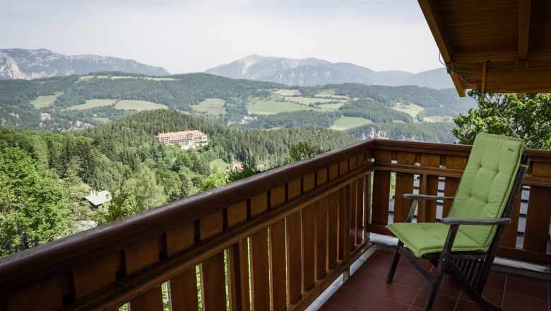 Aussicht vom Hotel, © Sebastian Freiler Blick von einem Balkon auf eine Berglandschaft mit Wäldern und einem Gebäude in der Ferne.