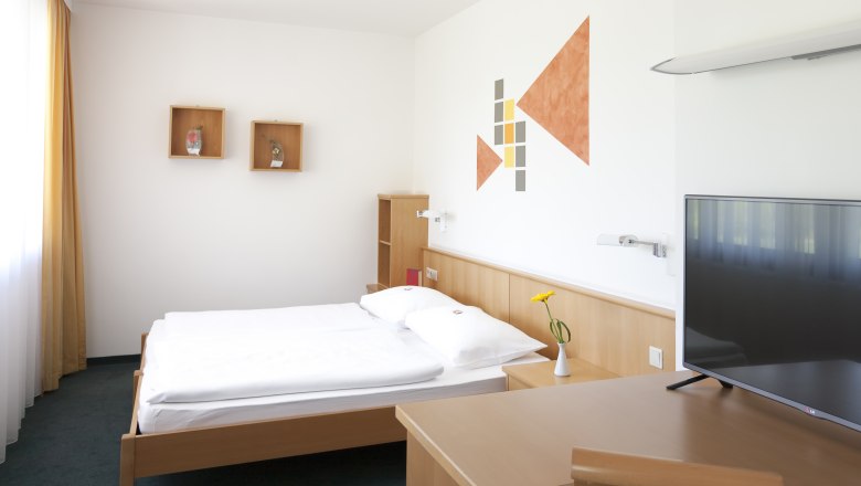 Zimmerblick, © missionINGE.com Modern eingerichtetes Hotelzimmer mit Bett, Schreibtisch, Fernseher und Wanddekoration.