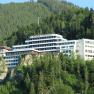 Das Sporthotel am Semmering, © Sporthotel Semmering Ein großes, modernes Hotelgebäude auf einem bewaldeten Hügel.