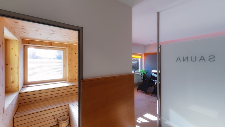 Sauna, © Hotel Belvedere/Gregor Hartmann Innenansicht einer Sauna mit Holzverkleidung und Fenster, daneben ein Ruheraum mit Liegestühlen.