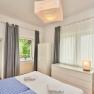 Top 2 - Schlafzimmer, © VP FeWo OG Helles Schlafzimmer mit Doppelbett, blauen Streifenbettwäsche, weißen Möbeln und grauen Vorhängen. Fenster mit Blick auf einen Balkon.