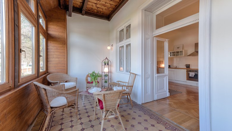 Top 1 - Wintergarten, © VP FeWo OG Wintergarten mit Holzwänden, Rattanmöbeln und Blick in eine Küche.