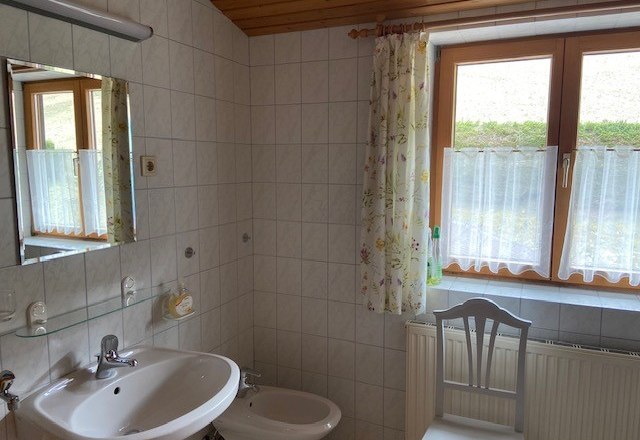 Badezimmer, © Wiener Alpen Ein Badezimmer mit Waschbecken, Bidet, Spiegel und Fenster mit Vorhängen.