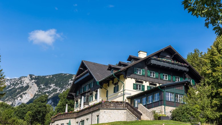 Ein traditionelles Gebäude in alpiner Umgebung mit blauen Himmel und Bergen im Hintergrund.