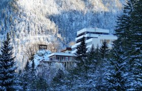 Winterliche Ansicht des Sporthotels Semmering umgeben von schneebedeckten Bäumen und Bergen.