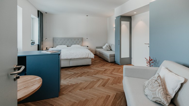 Modern eingerichtetes Hotelzimmer mit Doppelbett, Sofa und Holzboden.
