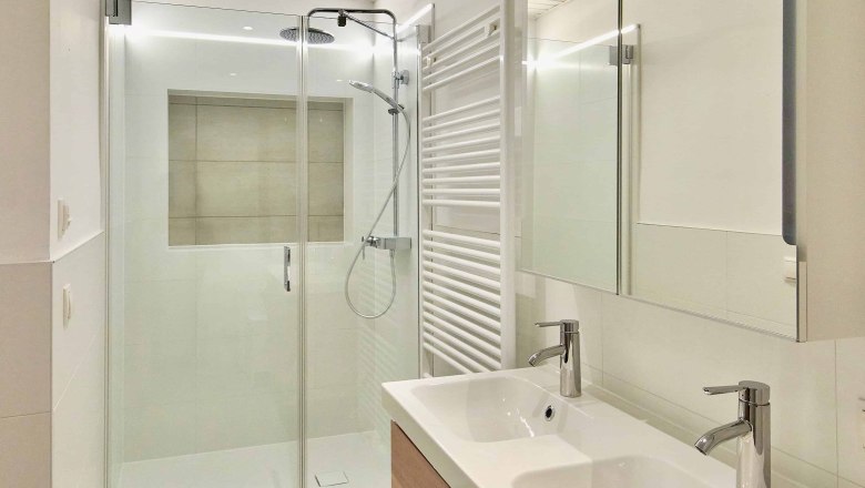 Modernes Badezimmer mit Doppelwaschbecken, Glasdusche und Handtuchheizkörper.