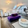 Modernes Loft mit violettem Sofa, Esstisch und K&uuml;che unter Dachfenstern.