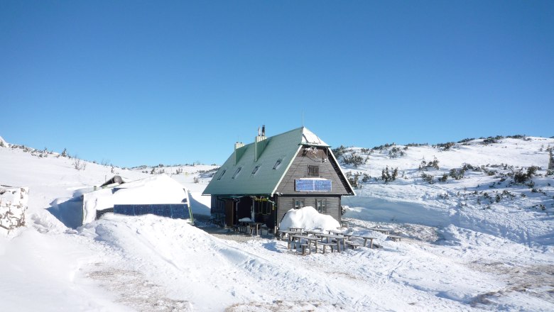 Eine Berghütte im Schnee mit Solarpanelen und blauem Himmel.