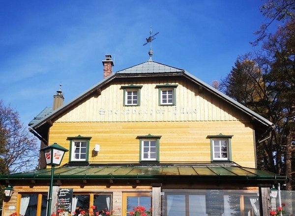 Holzhütte mit grünen Fensterläden und einem Wetterhahn auf dem Dach.