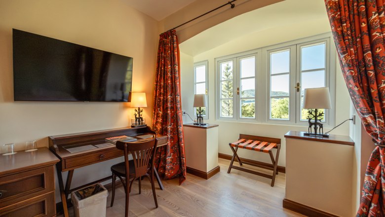 Hotelzimmer mit Schreibtisch, Stuhl, Fernseher und Fenster mit Aussicht.