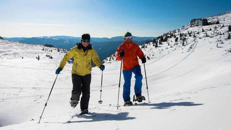 Zwei Personen beim Schneeschuhwandern in einer verschneiten Berglandschaft.
