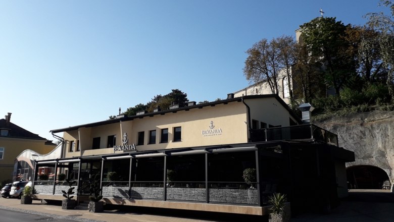 Gebäude mit der Aufschrift 'Bevanda' und Terrasse, umgeben von Bäumen und Felsen.