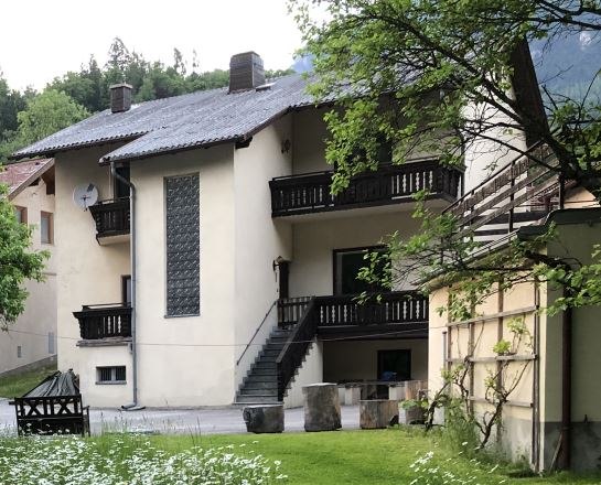 Ein zweist&ouml;ckiges Haus mit Balkon und Treppe, umgeben von einem gr&uuml;nen Garten mit Blumen.