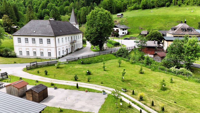 Landschaft mit historischem Gebäude, grünen Wiesen und Bäumen.