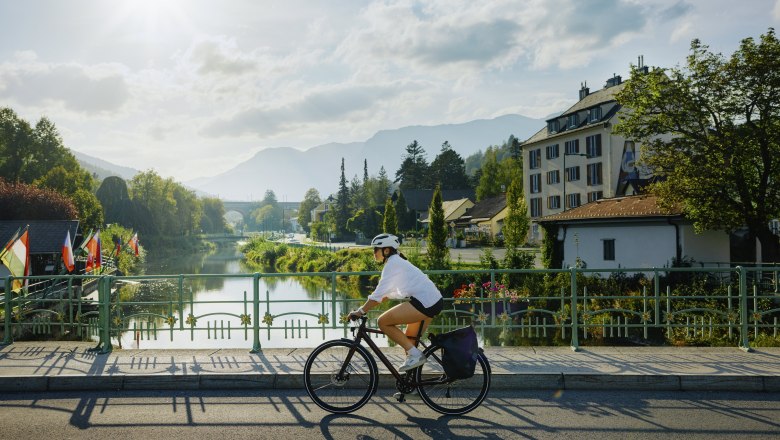 Frau auf dem Fahrrad, die über eine Brücke eines Flusses fährt