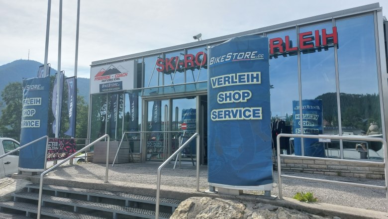 Eingang eines Sportgesch&auml;fts mit Verleih, Shop und Service. Im Hintergrund Berge.