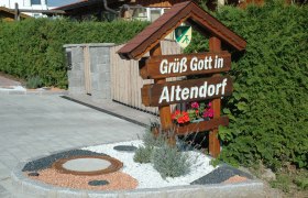 Willkommensschild mit der Aufschrift 'Gr&uuml;&szlig; Gott in Altendorf' vor einer Hecke.