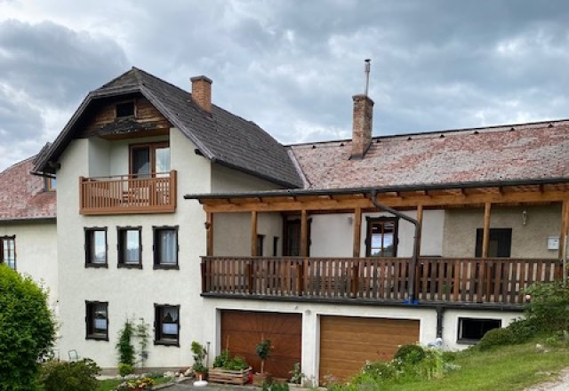 Ein zweistöckiges Haus mit Balkon und Garage, umgeben von grüner Landschaft.