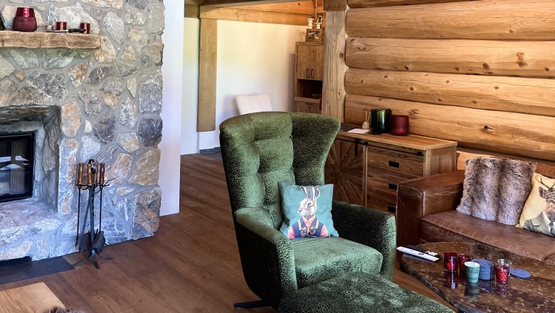 Gem&uuml;tliches Wohnzimmer mit Steinwand, Kamin, gr&uuml;nem Sessel und Holzm&ouml;beln.