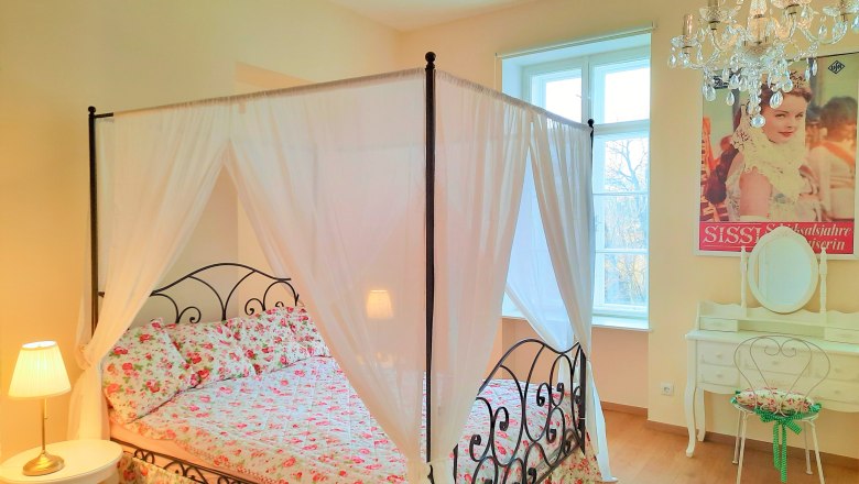 Schlafzimmer mit Himmelbett, Blumenbettw&auml;sche, Kronleuchter und Schminktisch.