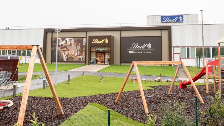 Spielplatz vor einem Lindt Factory Outlet mit Schaukeln und Rutsche.