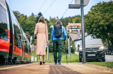 Zwei Personen am Bahnsteig, links der Zug und rechts ein Shuttlebus