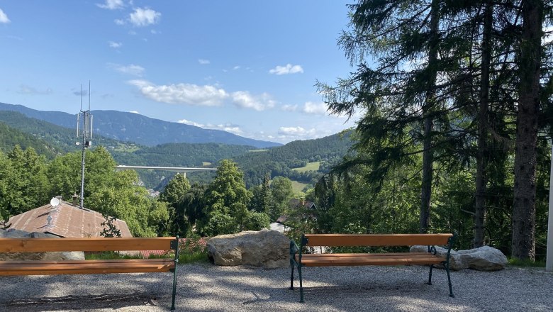 Zwei Bänke mit Blick auf eine Berglandschaft und eine Brücke.