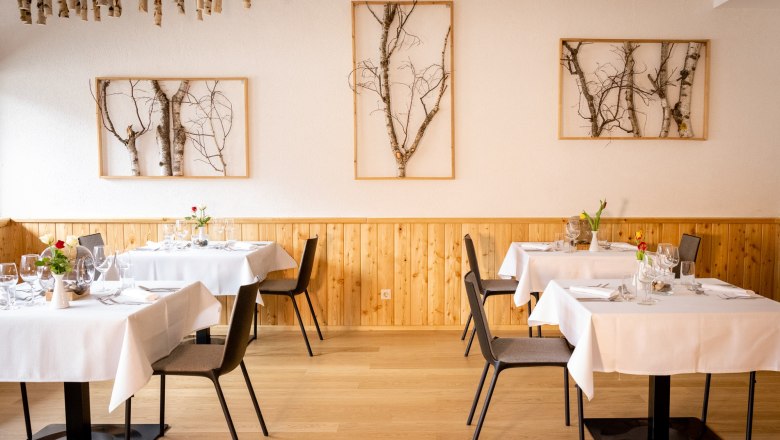 Elegantes Restaurant mit Holzw&auml;nden, wei&szlig;en Tischdecken und Birkenkunst an den W&auml;nden.